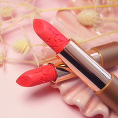 bright coral lipstick with gold accents on a pink floral background
