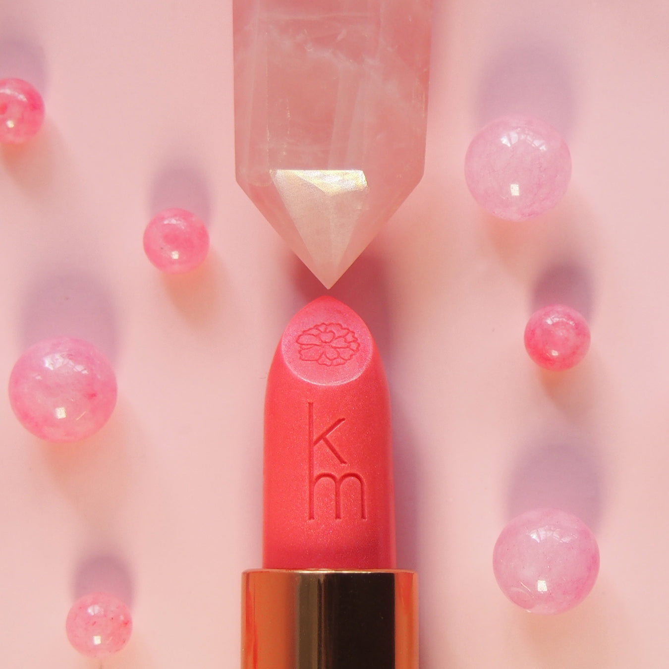 Pink lipstick with gold cap on a pink background with blurred pink beads